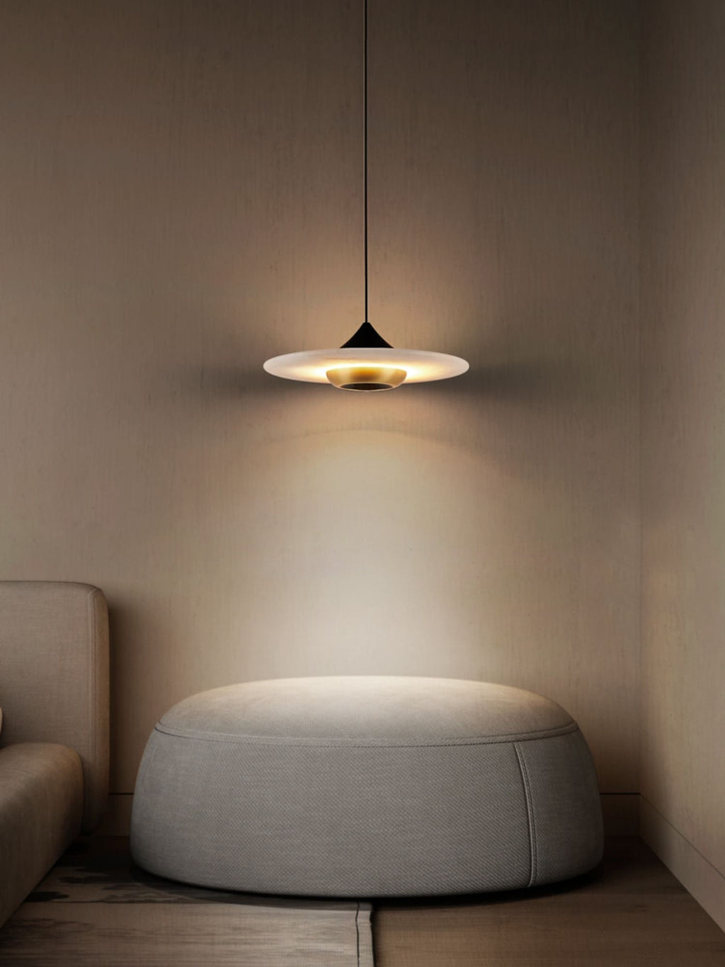 Clérachic Alabaster Disc Pendant Light lighting a round upholstered pouffe in a quiet corner beside a linen sofa.