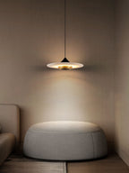 Clérachic Alabaster Disc Pendant Light lighting a round upholstered pouffe in a quiet corner beside a linen sofa.