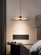 Clérachic Alabaster Disc Pendant Light over a bedside table with an open magazine and reading glasses.