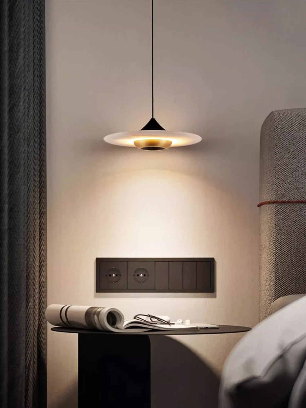 Clérachic Alabaster Disc Pendant Light over a bedside table with an open magazine and reading glasses.