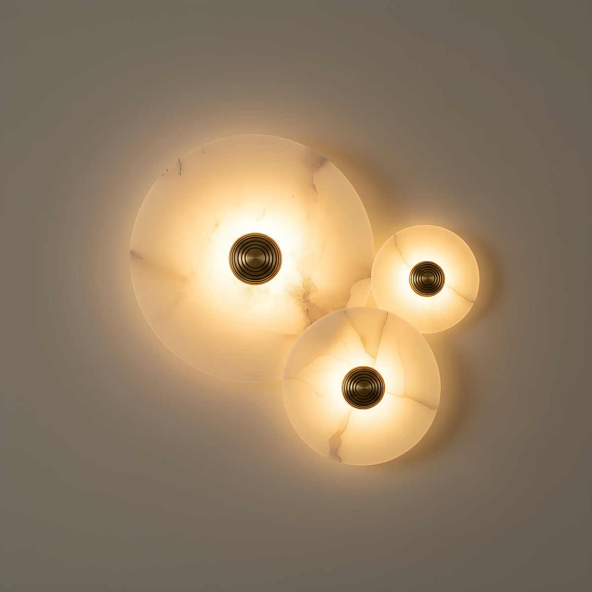 Three alabaster discs in mixed sizes mounted as an overlapping cluster, each lit from behind with its own brass boss, their light pooling together on the wall