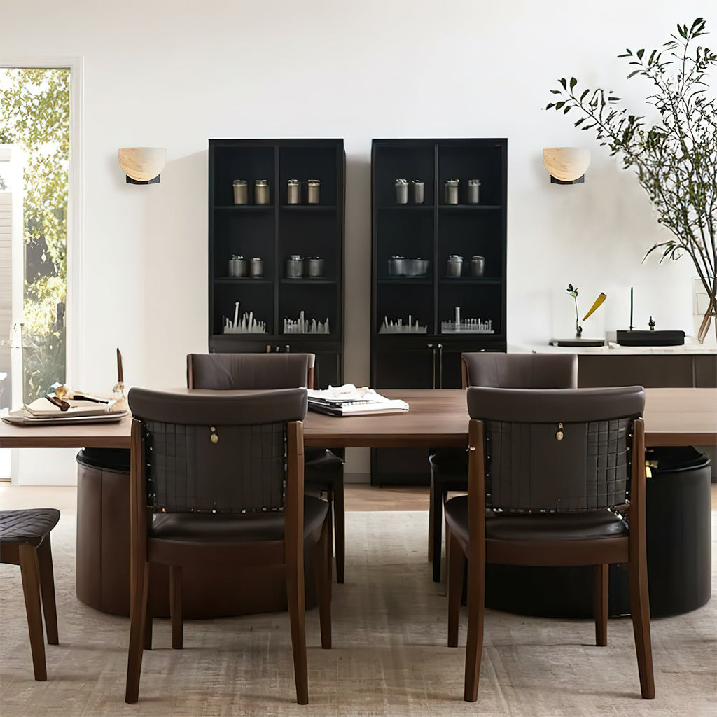 A pair of Clérachic alabaster wall lights flank a dark glass-fronted cabinet above a dining table with brown leather chairs.