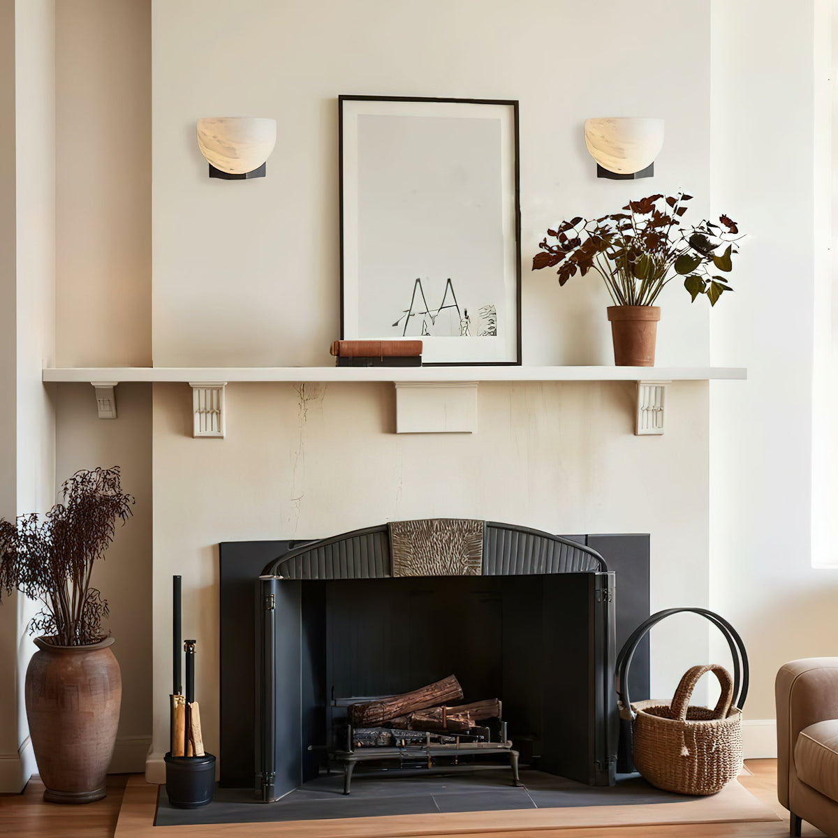 Two Clérachic alabaster wall lights hang either side of a framed print above a fireplace mantel, with a dried-flower vase on the hearth.