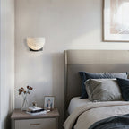 This Clérachic alabaster wall light with a dark bracket hangs above a bedside table and a grey headboard with navy cushions.