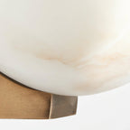 Close view of the cloudy alabaster dome of this Clérachic wall light where it meets its brushed brass bracket.