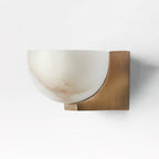 Front view of this Clérachic alabaster wall light, its half-dome shade curving into a brass bracket on a pale wall.