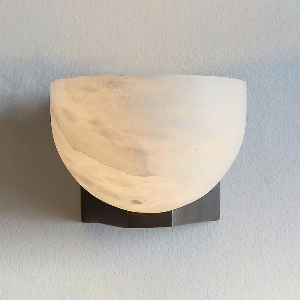 Lit alabaster dome of this Clérachic wall light glowing warm and cloudy against a grey-blue wall, on a dark bracket.