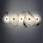 The Clérachic five-head alabaster sconce spans a grey wall, its stone shades glowing amber where light passes through.