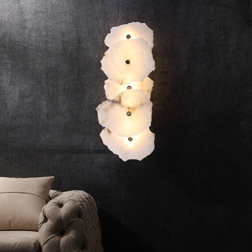 The Clérachic five-head alabaster sconce lit on a dark charcoal wall, with a sofa corner visible below.