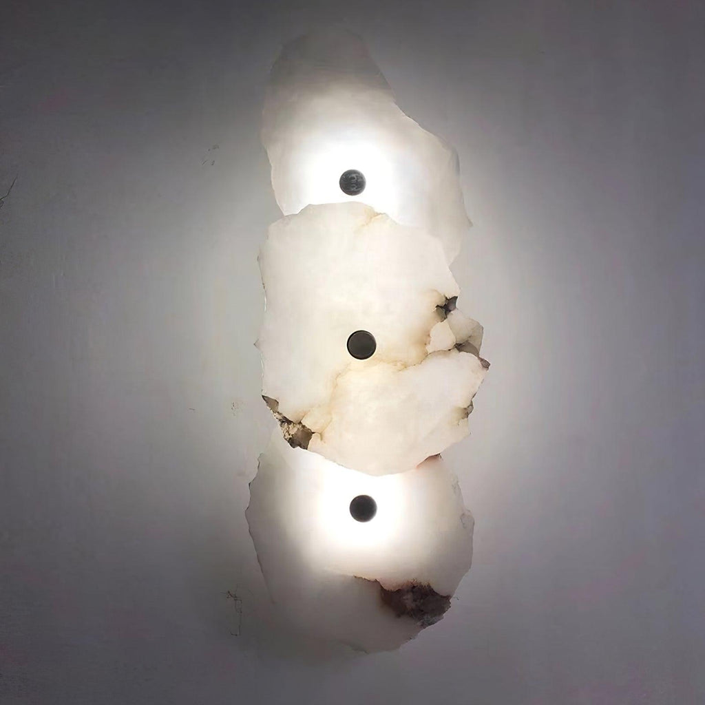 Clérachic's three-head alabaster wall lamp glowing brightly against a plain grey wall.