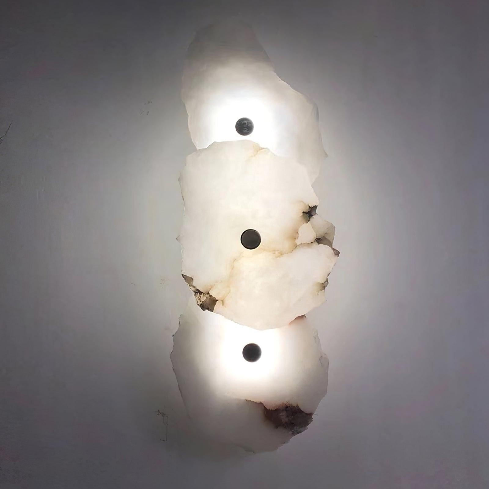 Clérachic's three-head alabaster wall lamp glowing brightly against a plain grey wall.