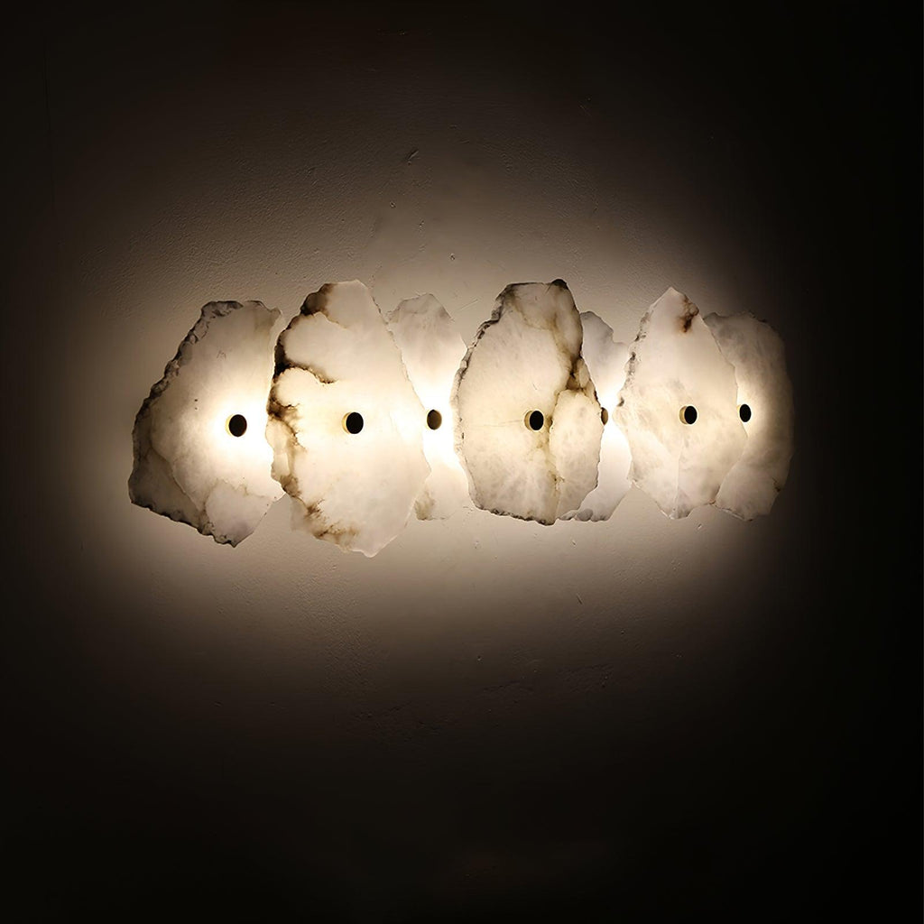 The Clérachic four-head alabaster sconce glows warmly against a dark background, showing its amber-toned edges.