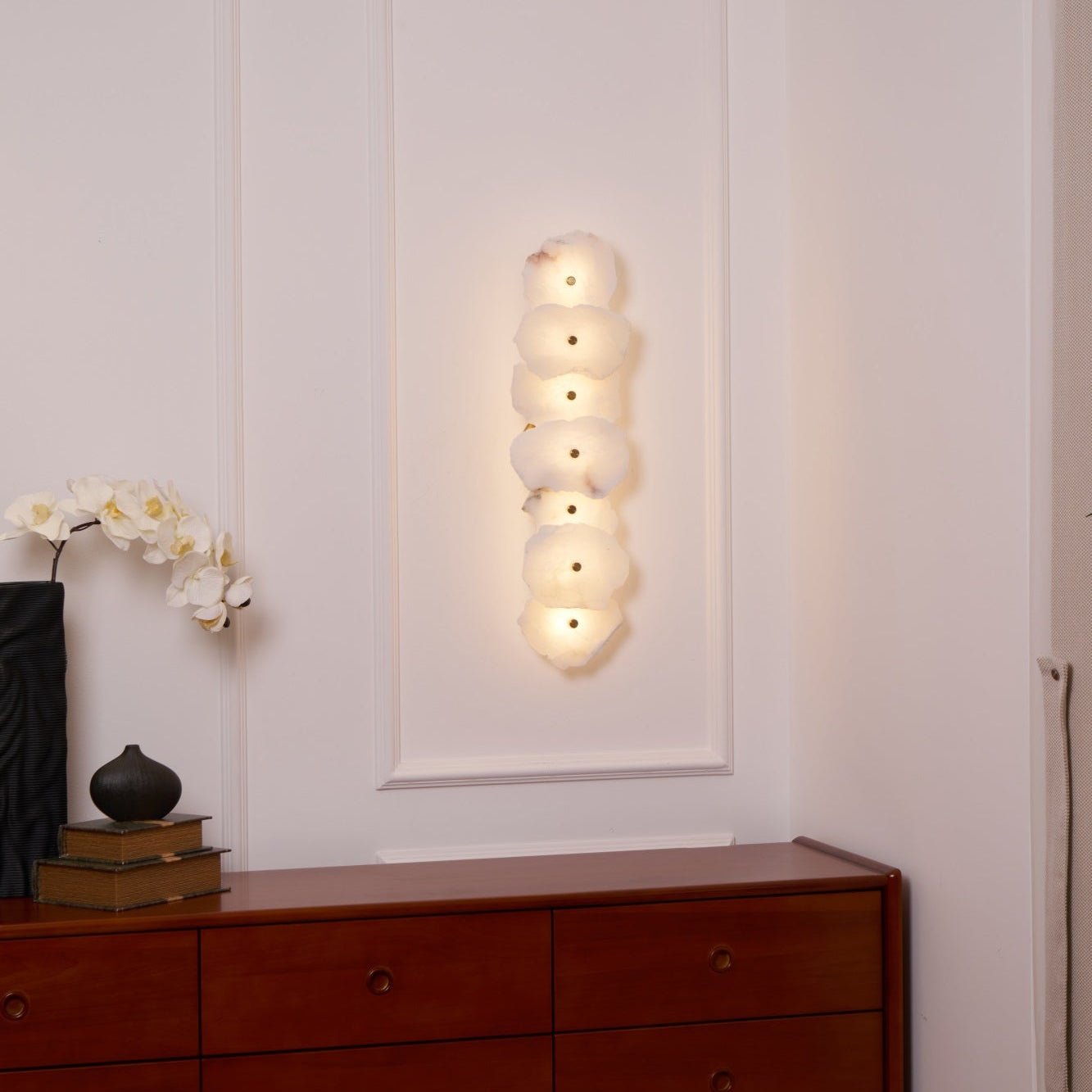 The Clérachic seven-head alabaster lamp lit in a wall alcove above a wood dresser and orchid.