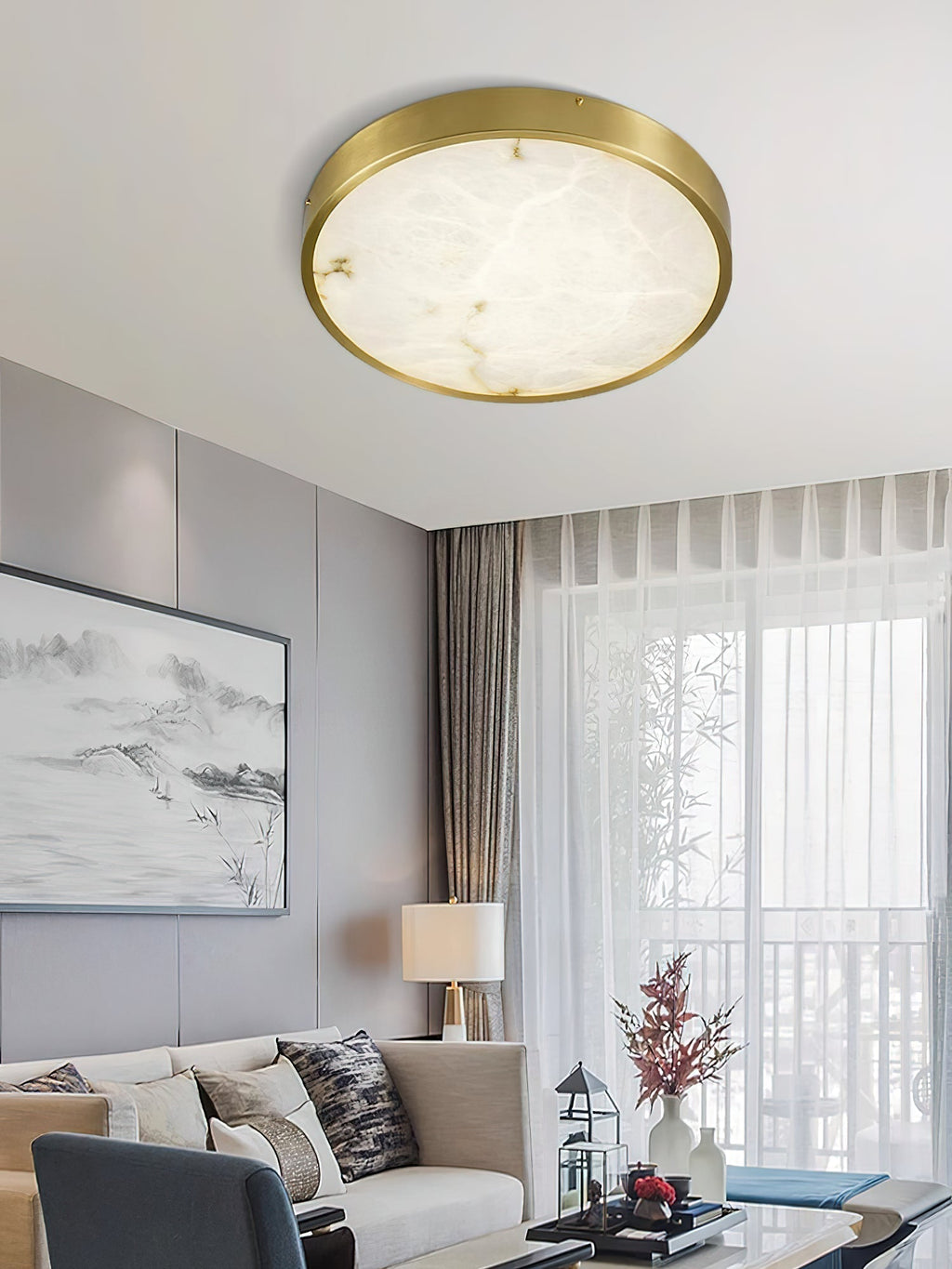 Round Clérachic alabaster flush ceiling light glowing above a living room sofa, artwork and a sheer-curtained window.