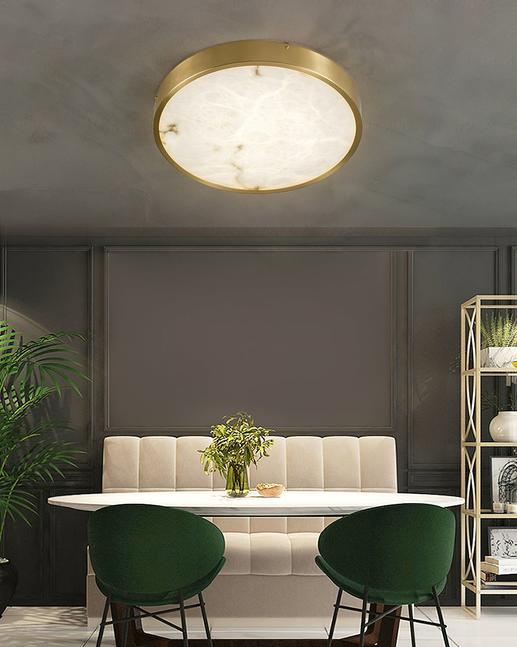 Round Clérachic alabaster flush ceiling light above a dining nook with a banquette, marble table and green velvet chairs.