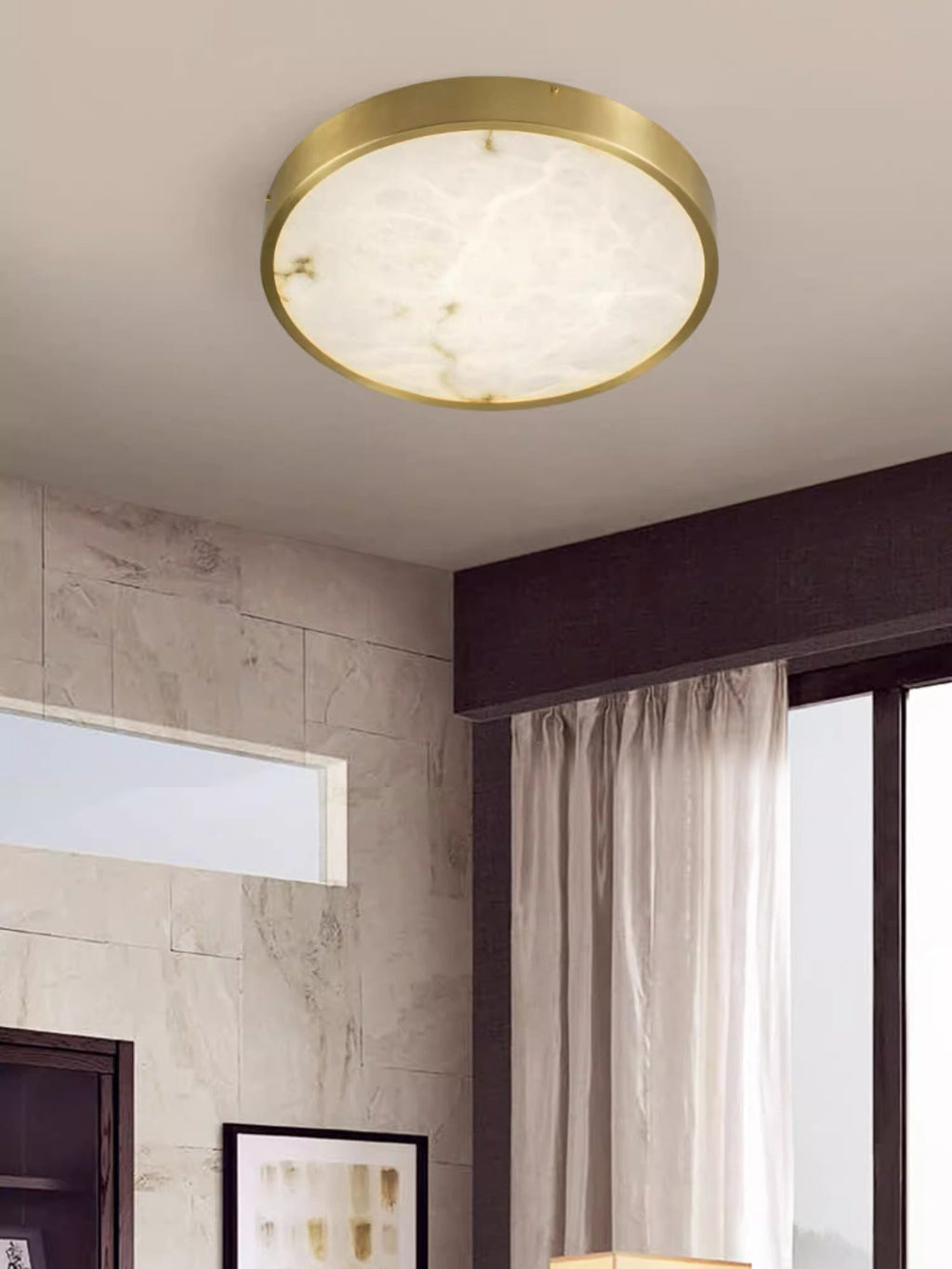 Clérachic alabaster flush ceiling light, round, lighting a corner where a stone-tiled wall meets a curtained window.