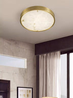 Clérachic alabaster flush ceiling light, round, lighting a corner where a stone-tiled wall meets a curtained window.
