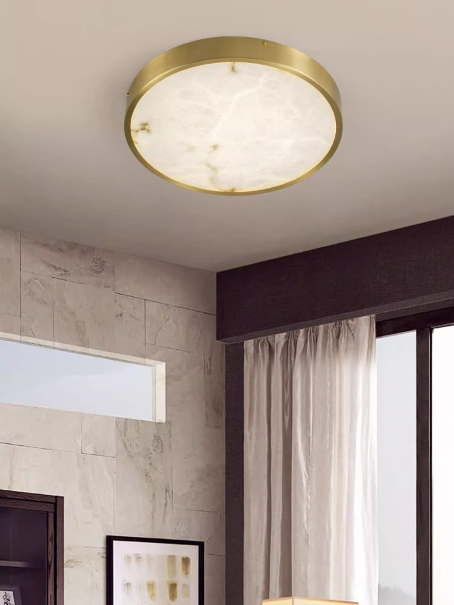 Clérachic alabaster flush ceiling light, round, lighting a corner where a stone-tiled wall meets a curtained window.