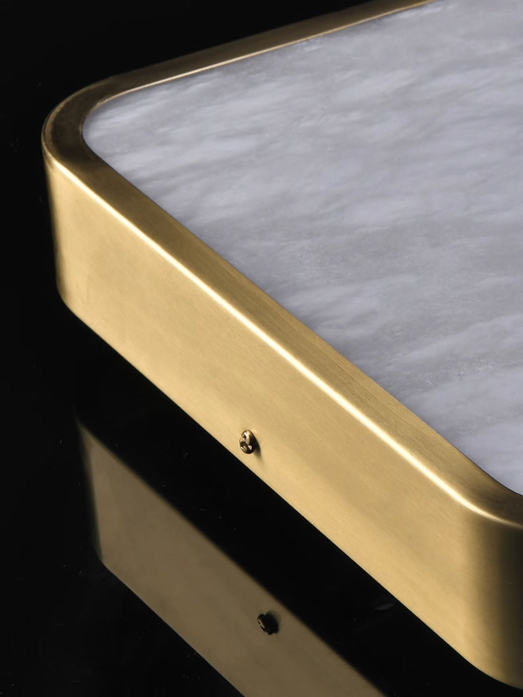 Corner detail of the Clérachic alabaster flush ceiling light, the brushed brass band and its fixing screw against the stone.