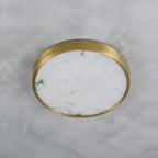 Round Clérachic alabaster flush ceiling light viewed straight up on a marble ceiling, brass band circling the stone face.