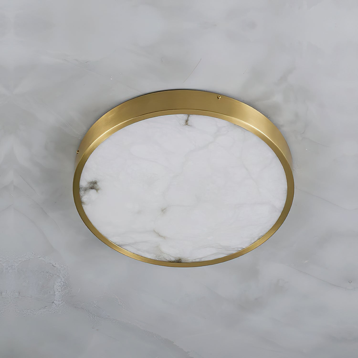 Round Clérachic alabaster flush ceiling light viewed straight up on a marble ceiling, brass band circling the stone face.
