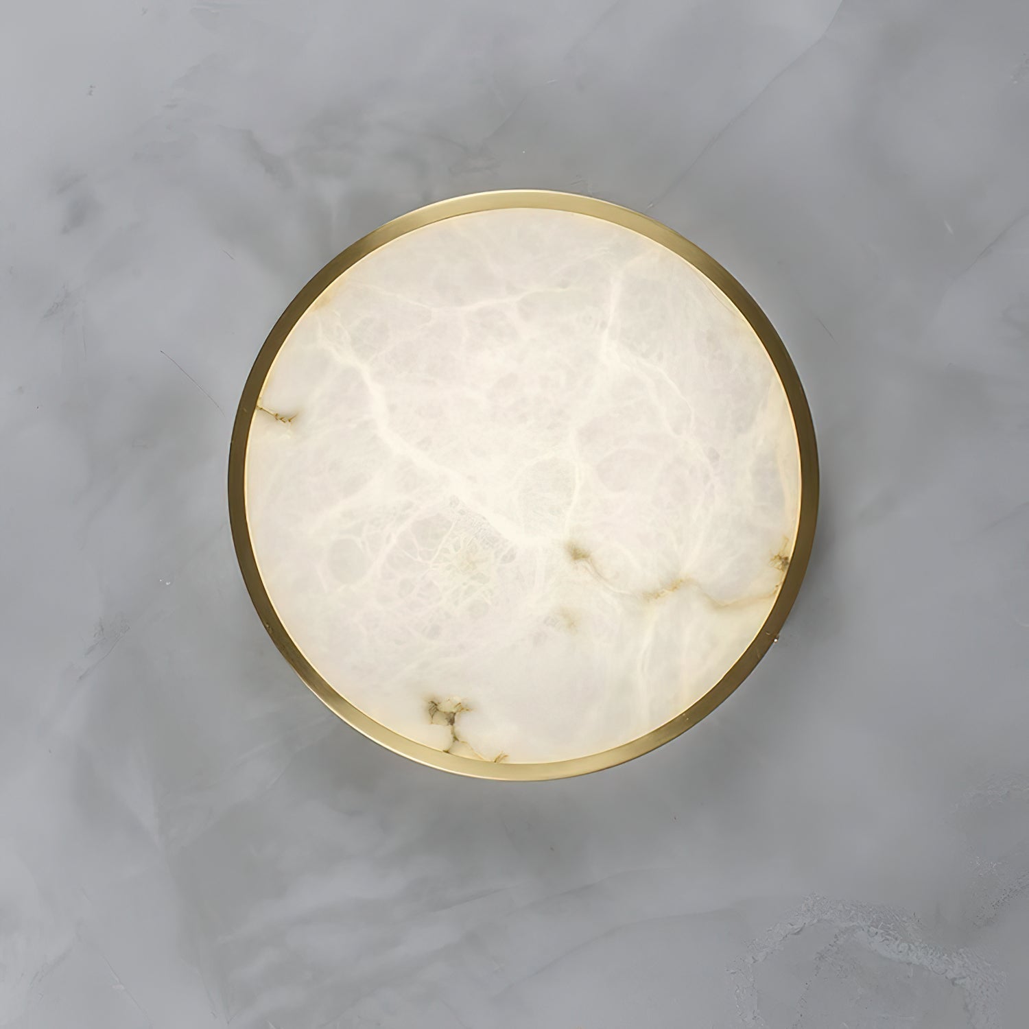 The alabaster face of the round Clérachic flush ceiling light fills the frame, its grey veining ringed by a thin brass rim.