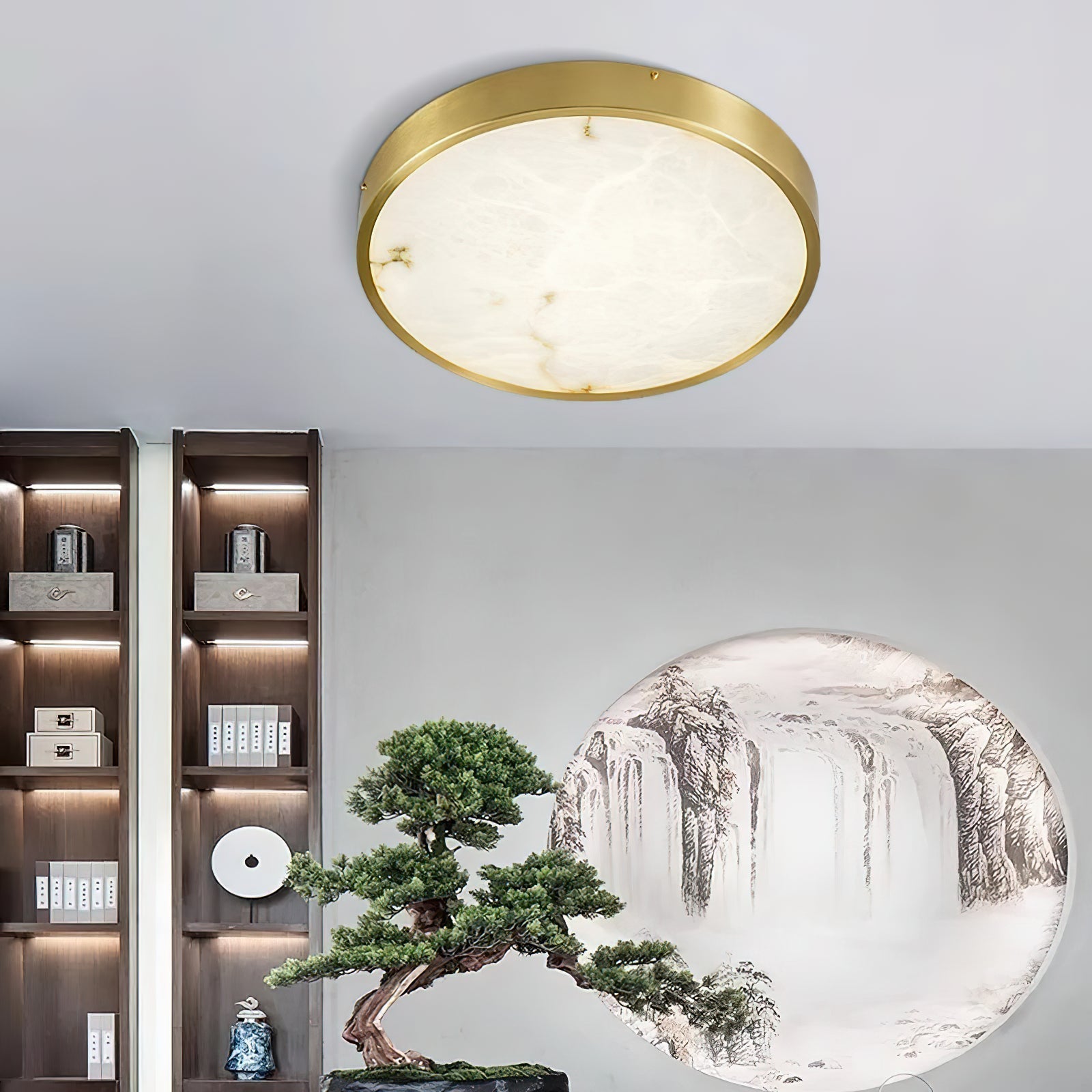 Round Clérachic alabaster flush ceiling light lighting a room with backlit shelving, a bonsai and a landscape mural.