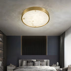 Round Clérachic alabaster flush ceiling light glowing over a bed against a deep blue wall with a fluted timber panel.