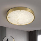 Clérachic alabaster flush ceiling light seen close in round form, lit above a fluted grey wall and a round mirror.