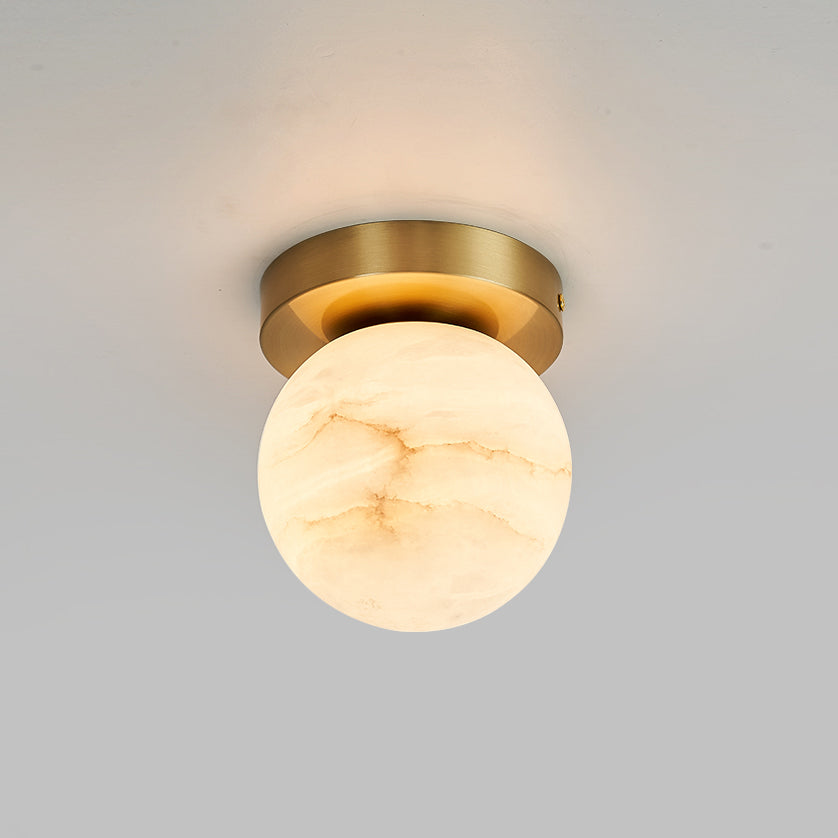 Globe-shade Clérachic flush mount ceiling light glowing softly against a smooth grey ceiling, brass canopy tight to the plaster