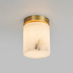 The cylinder version of the Clérachic alabaster ceiling light seen head-on, warm light filling the stone above a hallway