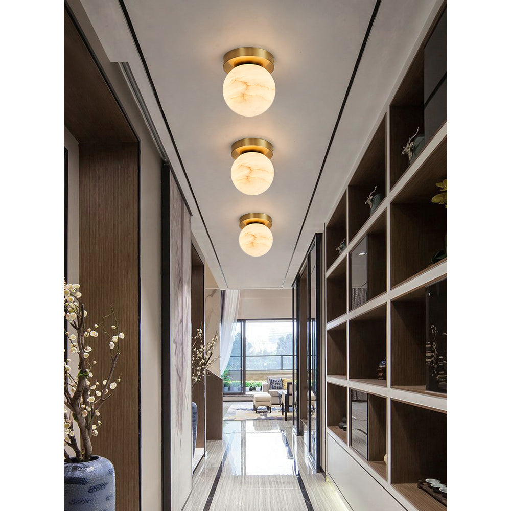 Three Clérachic alabaster globe ceiling lights in a row down a narrow hallway with dark wood shelving and a blossom branch