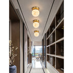 Three Clérachic alabaster globe ceiling lights in a row down a narrow hallway with dark wood shelving and a blossom branch