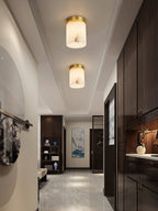 Two Clérachic alabaster cylinder ceiling lights lighting an entry corridor with dark cabinetry and a polished marble floor