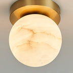 Close view of the Clérachic alabaster globe ceiling light, lit stone veining running across the shade below the brass canopy