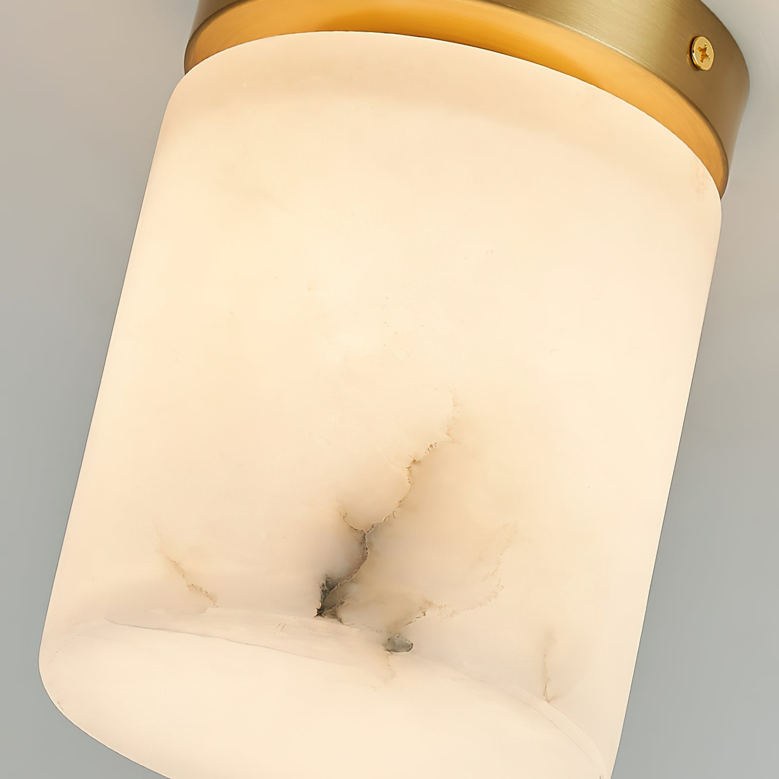 Detail of the Clérachic alabaster cylinder shade lit from inside, a dark grey vein and the domed base under the brass rim