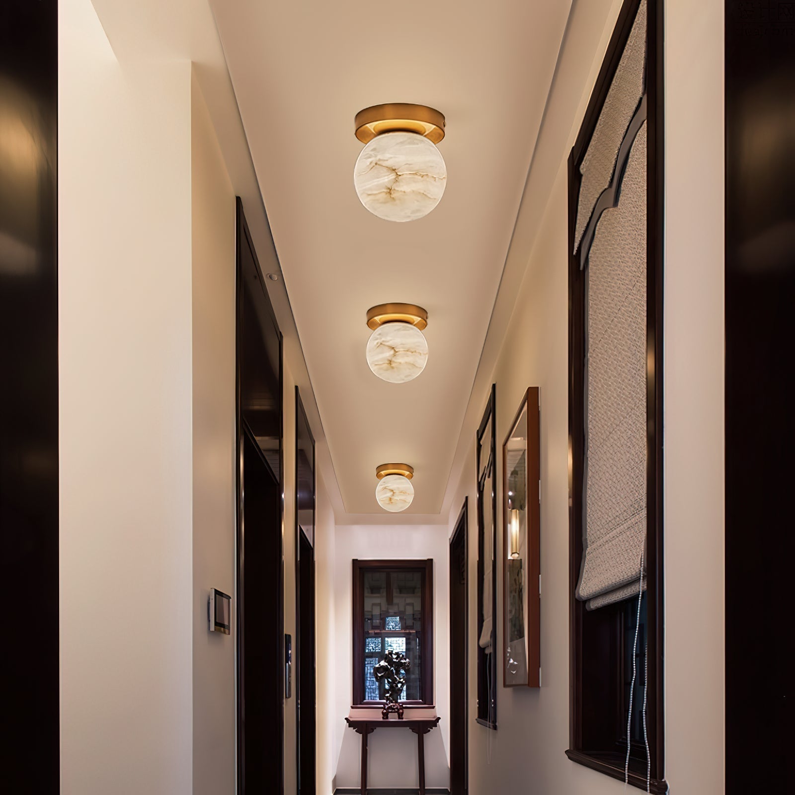 Three Clérachic alabaster globe ceiling lights down a narrow corridor hung with framed mirrors and a console table at the end