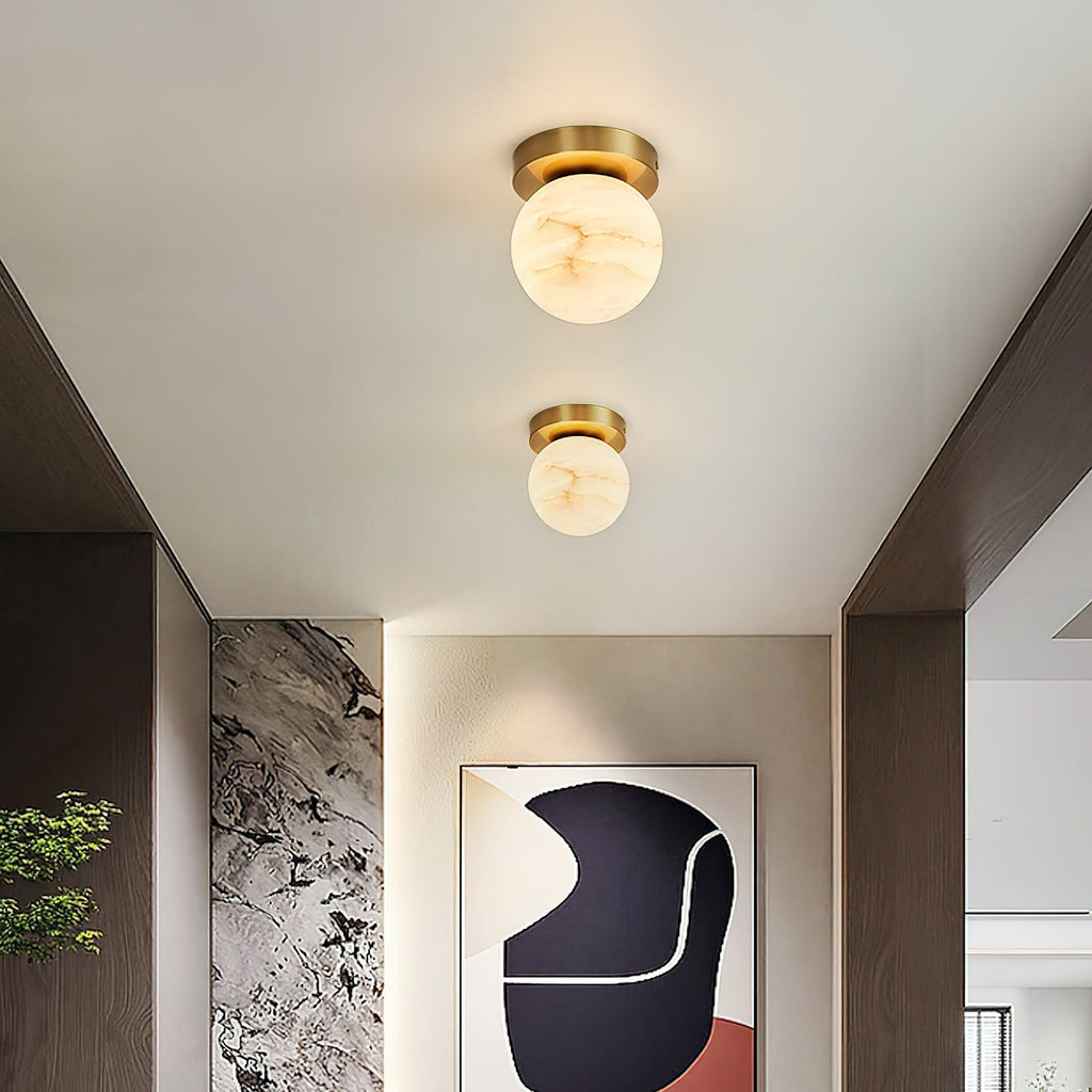 Two Clérachic alabaster globe ceiling lights above a hallway with a textured stone wall and a framed abstract print
