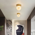 Two Clérachic alabaster globe ceiling lights above a hallway with a textured stone wall and a framed abstract print