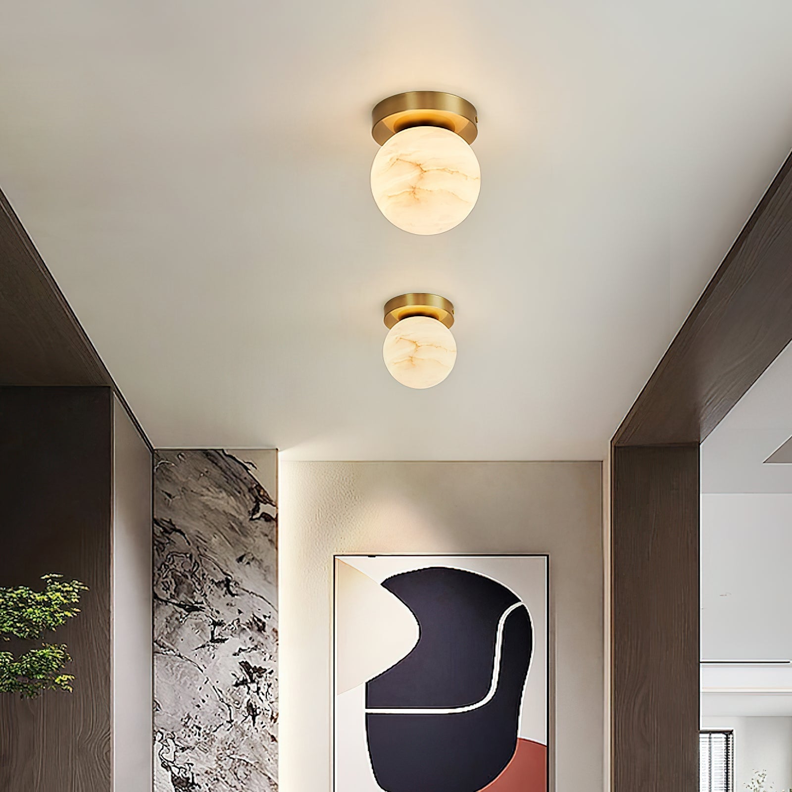 Two Clérachic alabaster globe ceiling lights above a hallway with a textured stone wall and a framed abstract print