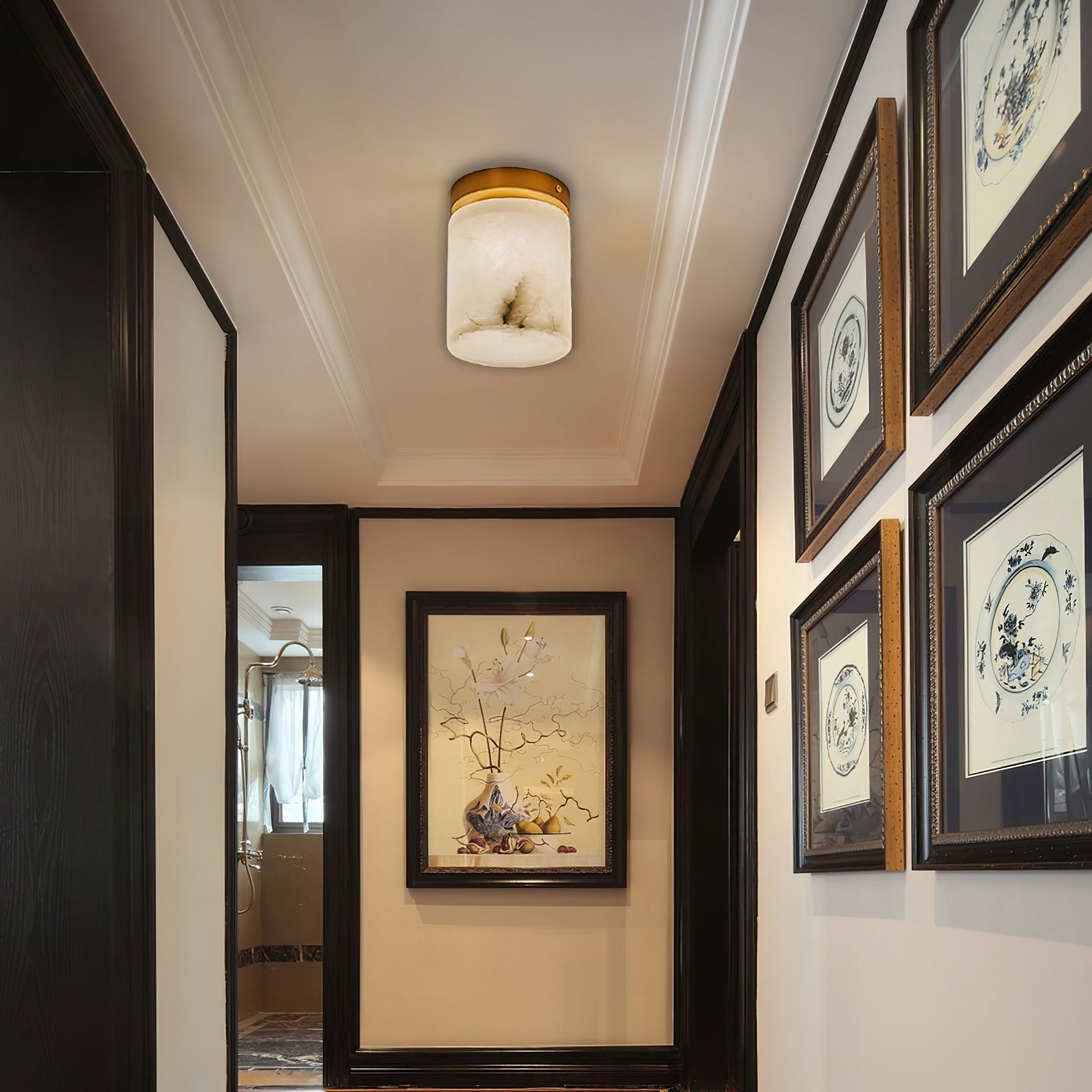 A Clérachic alabaster cylinder ceiling light glowing in a hallway lined with framed botanical prints and dark joinery