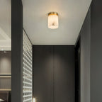 A single Clérachic alabaster cylinder ceiling light lighting a passage beside dark wood wardrobes and a white lattice screen