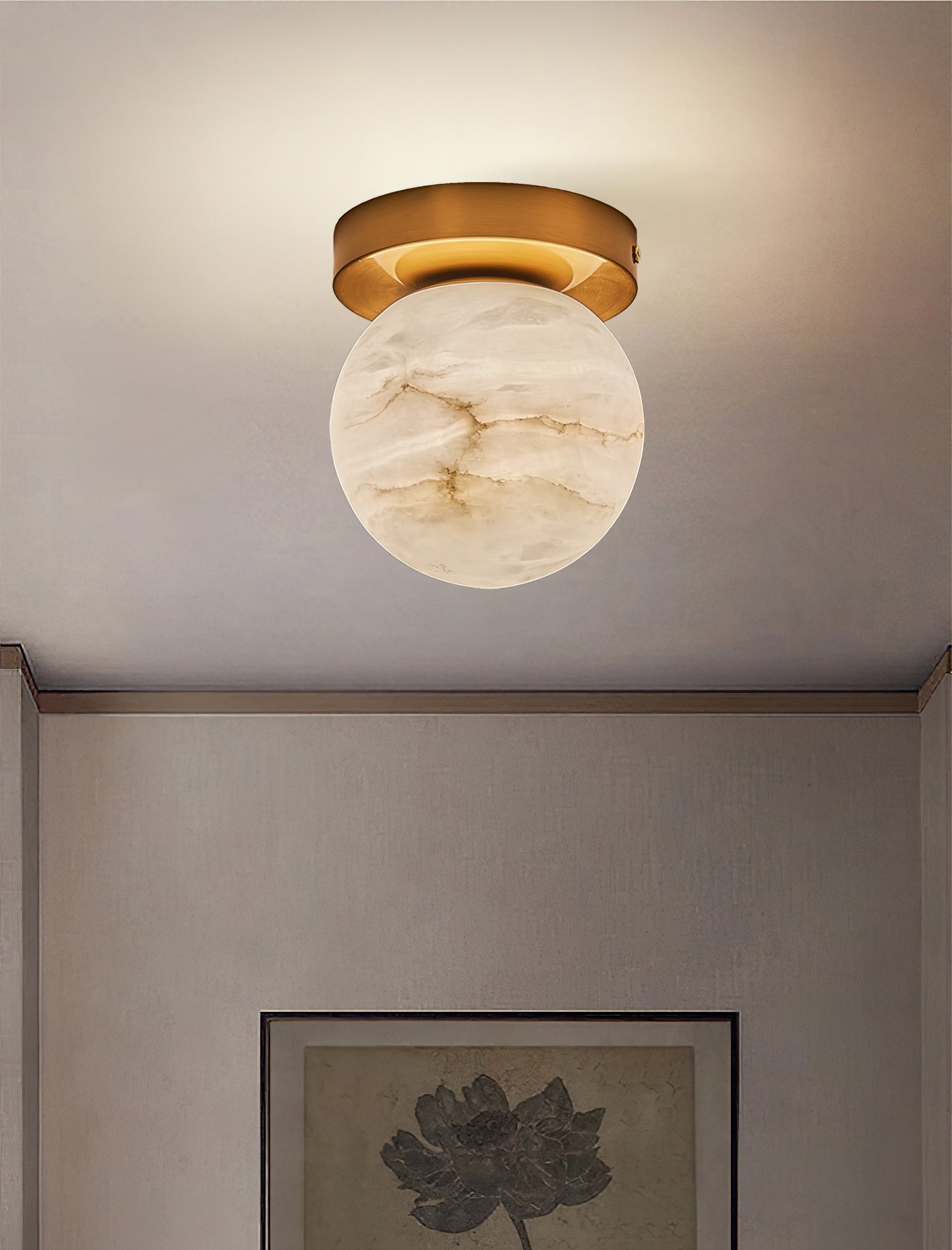 Clérachic alabaster globe ceiling light casting a soft wash across the ceiling above a framed lotus print in a quiet hall
