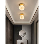 Two Clérachic alabaster globe ceiling lights in an entryway with a round mirror, dark panelling and a slim console