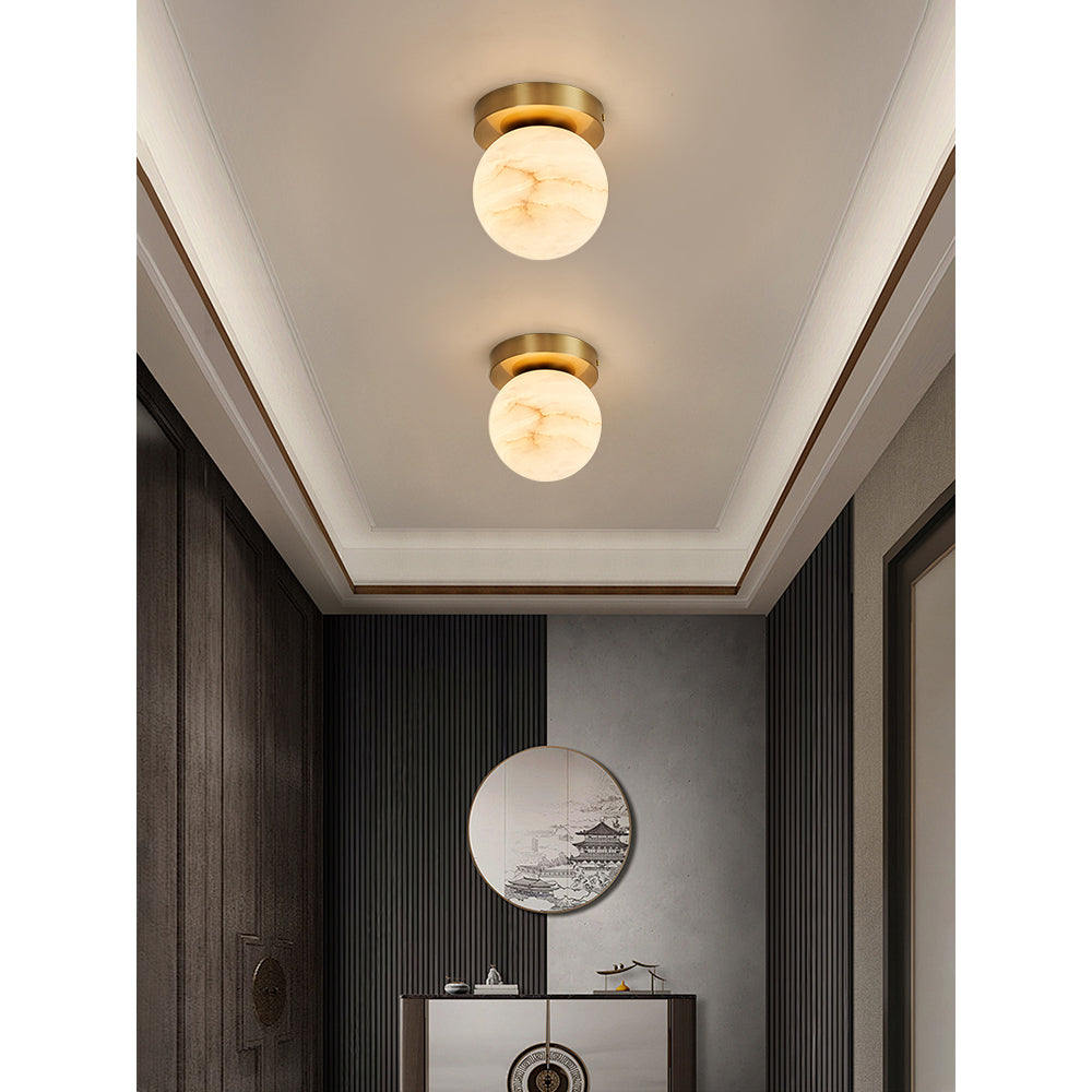 Two Clérachic alabaster globe ceiling lights in an entryway with a round mirror, dark panelling and a slim console