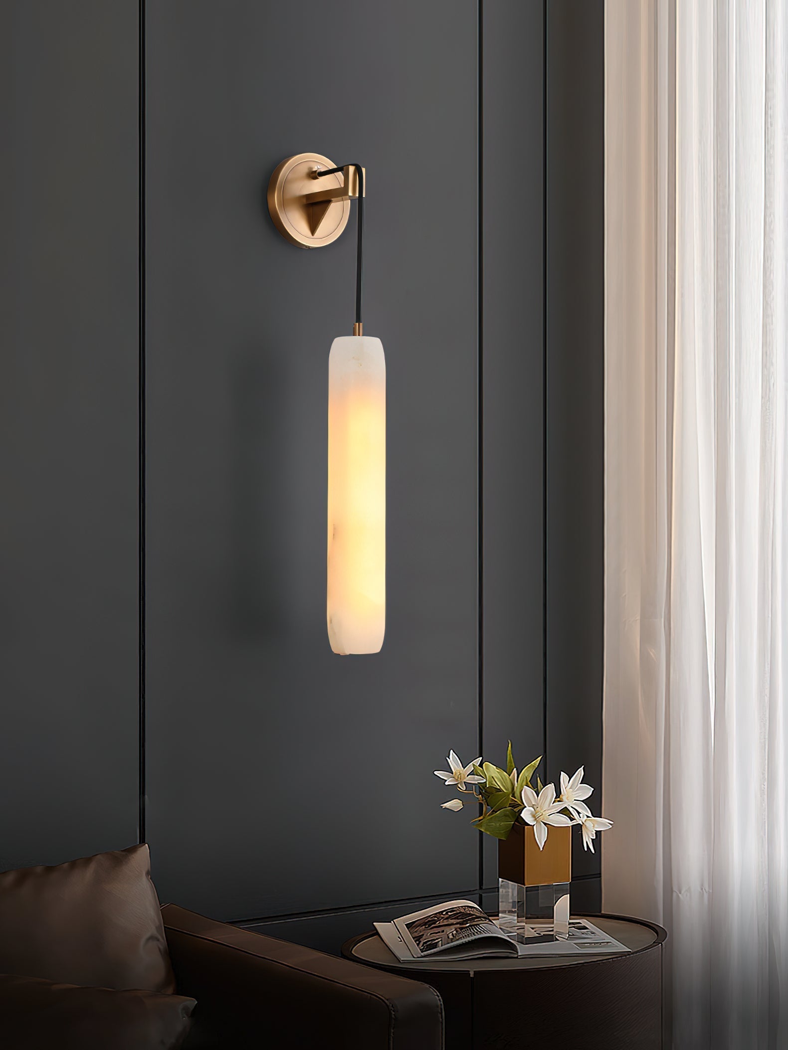 The Clérachic sconce warms a grey panelled corner above a side table with an open book and cut flowers.