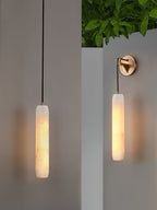 Clérachic alabaster flute shown as both a hanging drop and a wall-mounted sconce beside a planted white ledge.