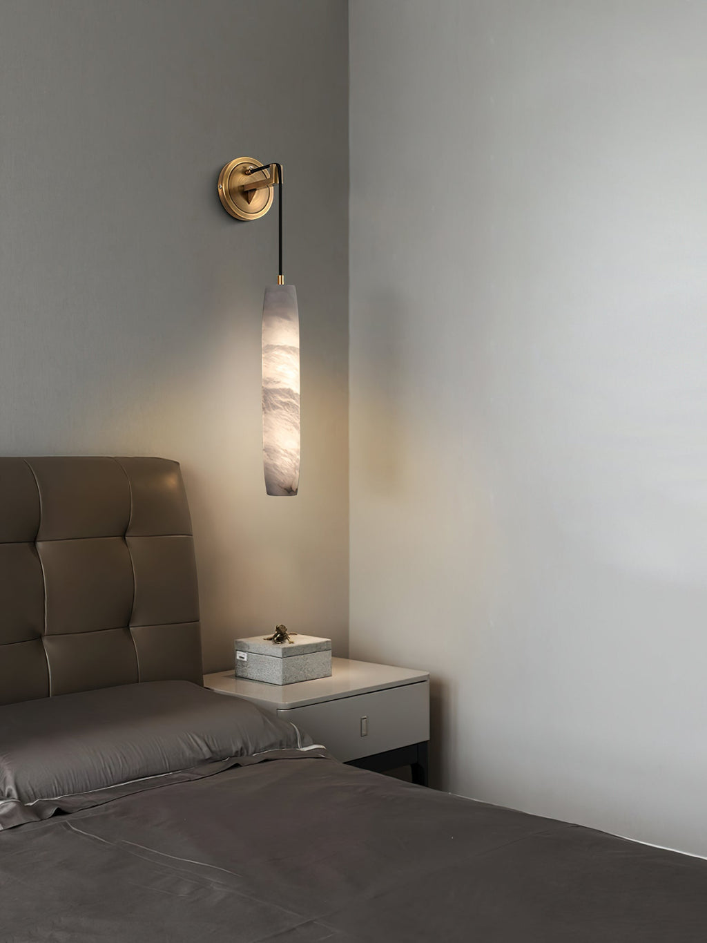 Clérachic sconce beside a tufted headboard, the alabaster column balancing a low nightstand in a grey bedroom.