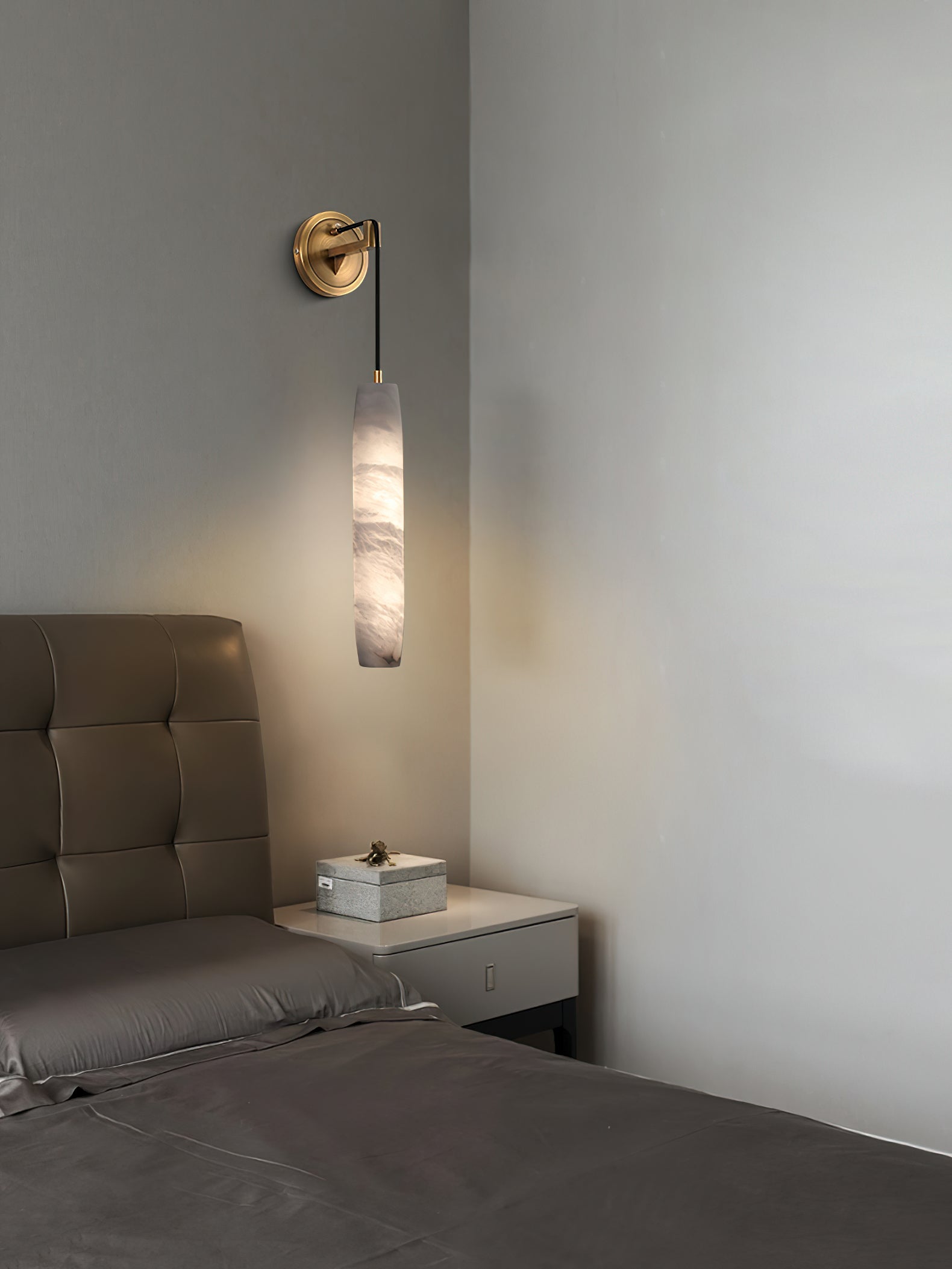 Clérachic sconce beside a tufted headboard, the alabaster column balancing a low nightstand in a grey bedroom.