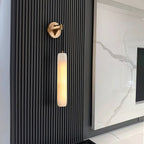The Clérachic sconce on a black fluted timber wall, its warm column set against a veined marble media panel.